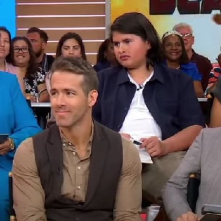 Julian Dennison is sitting behind Ryan Reynolds as they are looking at the interviewer.